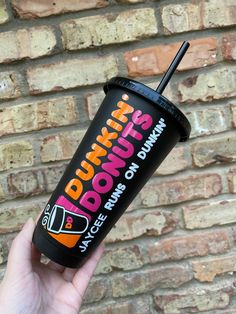 a person holding up a drink in front of a brick wall with the words dunkin'donuts on it