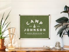 a camp sign hanging on the wall next to potted plants