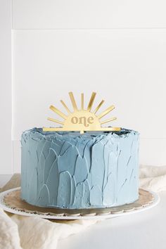 a blue cake sitting on top of a table next to a white plate with a gold one sign