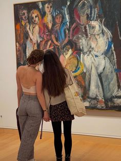 two women standing in front of a painting looking at each other's butts