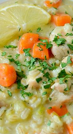 a white bowl filled with chicken and rice soup next to lemon wedges on the side