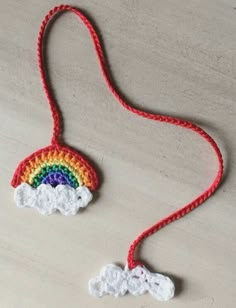 a crocheted rainbow and cloud decoration hanging from a red string