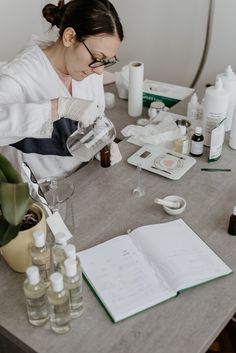 a woman in glasses is doing something on a table with bottles and other items around her