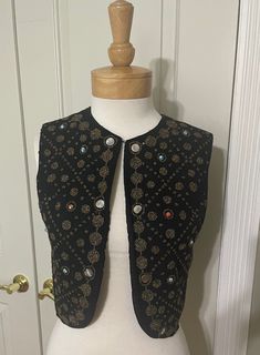 Embellished and exotic women's vest from the 1960's.  The piece is made from black wool knit and is completely lined with a solid black taffeta. There is a hook and eye closure at the front neck.   The bronze seed beads appear to have been glued into place (as opposed to sewn). The lattice style design is also embellished with dime sized mirrored silver sequins and plastic marbleized beads in tones of turquoise and coral.  Some of the sequins are slightly curled, perhaps from dry cleaning - but otherwise the beads are in excellent condition, with none of them missing.  I imagine this piece was probably hand crafted at home.  The back of the vest is a solid black wool.  No holes or stains to note -and no label.  Very good to excellent vintage condition. Bust:   38" Armhole:  18" Length at c Winter Bohemian Black Vest, Traditional Black Sleeveless Vest, Embellished Bohemian Sleeveless Vest, Fitted Bohemian Vest For Party, Bohemian Fitted Vest For Party, Traditional Black Vest For Festival, Fitted Embellished Vest For Fall, Traditional Fitted Black Vest, Festive Vintage Fitted Vest