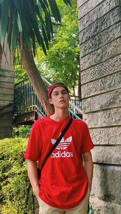 a young man standing next to a palm tree wearing a red adidas t - shirt