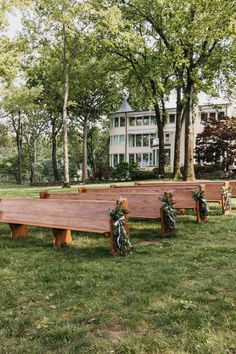 an outdoor ceremony setup with wooden benches and greenery on the grass in front of a large building