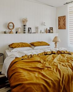 a bed with gold sheets and pillows in a white room next to a wall mounted shelf