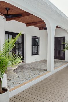 a white house with wooden floors and ceiling fans on the roof, along with potted plants