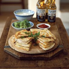 a wooden table topped with lots of food next to bottles of beer and sauces