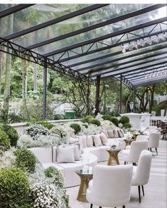 a room filled with lots of white couches and tables covered in greenery next to trees