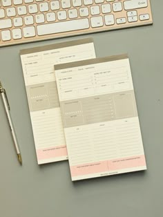 two notebooks sitting next to a keyboard on top of a desk with a pen