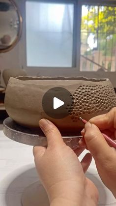 a woman is working on a clay bowl with her hands and fingers, while another person holds