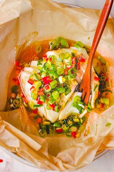 a bowl filled with soup and vegetables on top of a wooden spoon in some brown paper