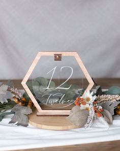 the table numbers are displayed in an octagonal wooden frame with greenery and foliage around it