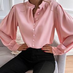 a woman sitting on a couch wearing a pink shirt and black pants with her hands on her hips