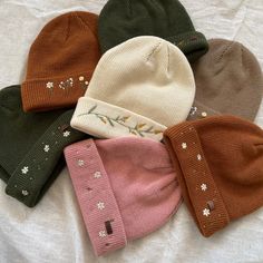 five knitted hats laid out on a white sheet, all with different designs and colors