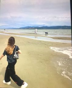 a woman is walking along the beach with her dog