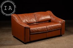 a brown leather couch sitting on top of a cement floor next to a black wall