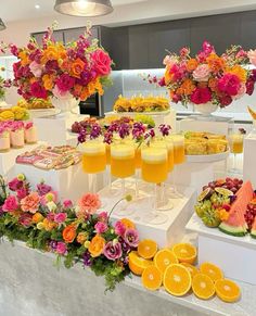 an assortment of fruits and flowers on display at a buffet table with champagne flutes in front of them