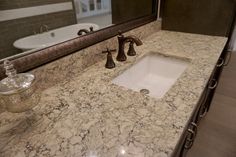 a bathroom sink with marble counter top and white bathtub in the backround