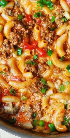 a skillet filled with pasta and meat covered in sauce, green onions and parsley