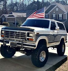 an old ford bronco truck with the american flag on it's hood parked in front of a house