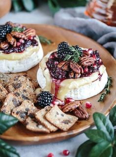 two cheeses with berries and pecans are on a plate next to crackers