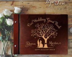 a wooden wedding guest book with a tree on it and two white roses in the foreground