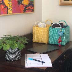 two baskets on a desk with a pen and paper in front of them next to a potted plant