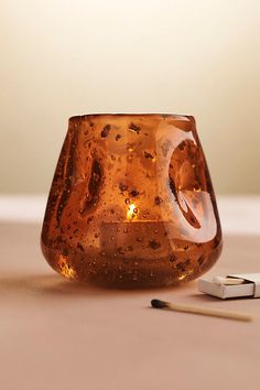 a glass candle holder sitting on top of a table next to a pencil and eraser