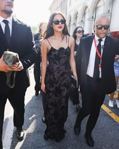 a woman in a black dress is walking down the street with two men behind her