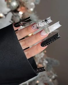 a woman's hand with black and white nail polish holding scissors in front of a christmas tree