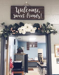 a welcome sign is hanging on the front door of a shop with flowers and greenery