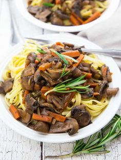 two white plates filled with mushroom pasta and carrots on top of a wooden table