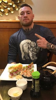 a man sitting at a table with food in front of him and pointing to the side