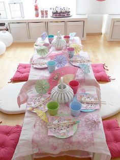 the table is set with pink and white plates, napkins, cups, and fan