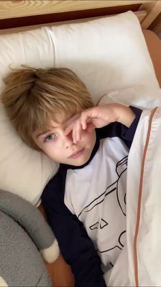 a young boy laying in bed with his hand on his forehead and looking at the camera