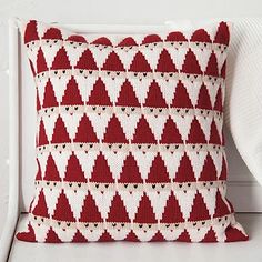 a red and white knitted pillow sitting on top of a white chair next to a wall