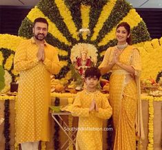 two people and a child standing in front of a flower display with yellow flowers on it