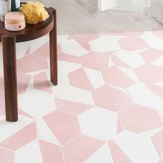 a bathroom with pink and white tiles on the floor next to a wooden table topped with flowers