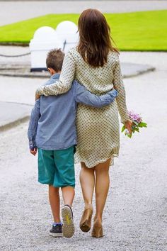 a woman walking down a path with a young boy holding her arm around her back