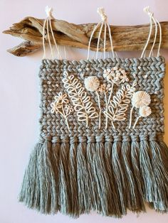 a wall hanging made out of yarn with flowers and leaves on the front, along with twine of driftwood sticks