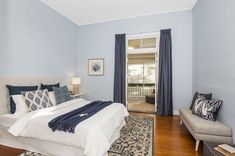 a bedroom with blue walls and wood floors has a bed, two chairs, and a rug on the floor