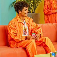 a man in an orange outfit is sitting on a couch and holding a can of soda