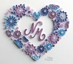 a heart made out of paper with the letter m in it's center surrounded by flowers