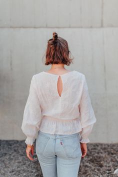 a woman standing in front of a wall wearing jeans and a white top with an open back