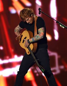 a man with tattoos on his arm and guitar in front of a microphone at a concert