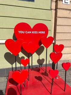 several red hearts are placed in front of a building with a sign that says you can kiss here