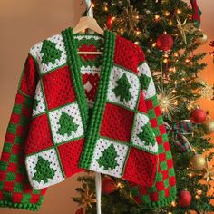 a red and green knitted christmas sweater hanging on a rack next to a tree