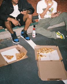 two young men sitting on the ground eating pizza